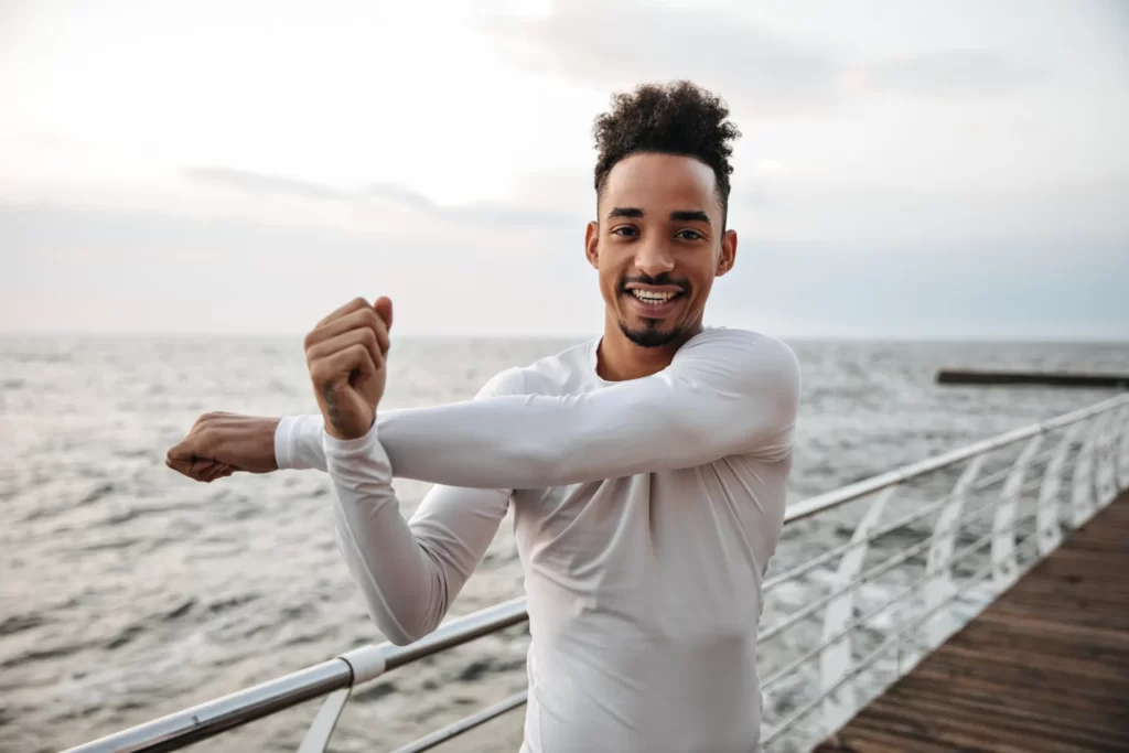 man stretching arms on wooden pier by ocean utc